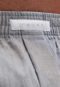 Tissu gris à motif chevron avec une ceinture élastique, comportant une étiquette blanche marquée "FALKE" en lettres argentées.