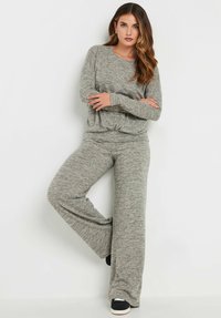 Completo da loungewear grigio composto da una maglietta a maniche lunghe con vestibilità comoda e nodo frontale, abbinata a pantaloni larghi; tessuto lavorato a maglia morbido e testurizzato.