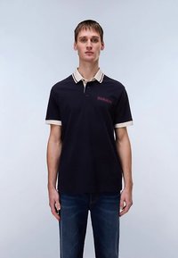 Μπλε ναυτικό πόλο με αντιθετικό μπεζ γιακά και τελειώματα στα μανίκια, με διακριτικό κόκκινο λογότυπο στο στήθος. Κατασκευασμένο από υφασμένο βαμβάκι.