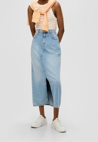Denim midi sukně v světle modré barvě s předním rozparkem, vysokým pasem a dvěma bočními kapsami. Vybavená bílým a oranžovým pruhovaným tílkem a bílými teniskami.