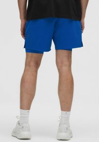 Blå idrottsshorts med en slät textur, två sidoklipp och en platt elastisk midja, tillsammans med vita sneakers och strumpor.