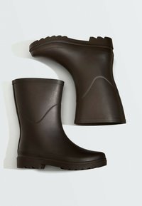 Paire de bottes de pluie en caoutchouc marron foncé avec semelles texturées, une botte debout et l'autre couchée sur le côté sur un fond clair.