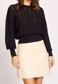 Svart stickad tröja med en lös, strukturerad design, långa ärmar och ribbade ärmslut; ihop med en krämfärgad läderminikjol.