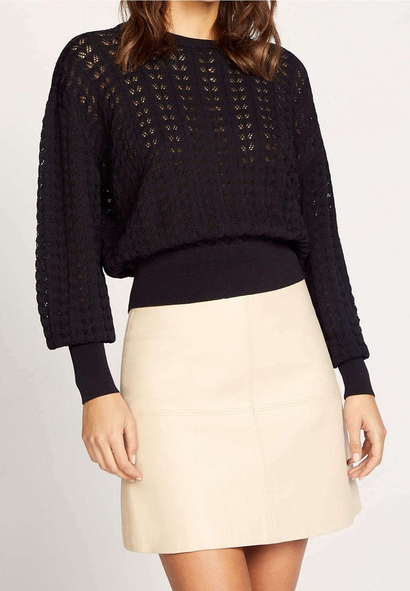 Svart stickad tröja med en lös, strukturerad design, långa ärmar och ribbade ärmslut; ihop med en krämfärgad läderminikjol.