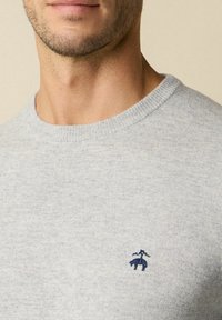 Grijze gebreide trui met een ronde hals en geribbelde manchetten, met een klein marineblauw geborduurd ontwerp op de linkerkant van de borst.
