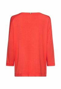 Koralfarvet oversized top med trekvartslange ærmer, rund hals og glat bomuldsstof. Enkel design med lige kant og split i ryggen.