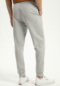 Szare spodnie dresowe z miękkiego materiału, z zwężanymi nogawkami, elastycznym pasem i kieszeniami bocznymi. Połączone z białymi trampkami.