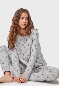 Conjunto de pijama gris con mangas largas y pantalones, que presenta un patrón de conejito y zanahorias. Fabricado con un material suave y ligero.