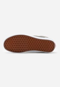 Podeszwa sneakersów z teksturowanym brązowym wzorem z gumy, białymi krawędziami i małym czerwonym akcentem. Powierzchnia posiada wzór o diamentowym chwycie.