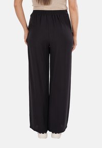 Pantaloni neri a gamba larga con vita elastica, realizzati in un tessuto leggero e liscio con una leggera texture. Nessuna tasca visibile o decorazioni.