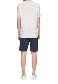 Camiseta de algodón blanca con mangas cortas, corte relajado, combinada con pantalones cortos azul marino y zapatillas blancas; diseño sencillo, sin patrones ni acentos visibles.