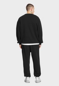 Czarny, oversize sweatshirt i pasujące dresy z miękkiego materiału. Projekt z okrągłym dekoltem, z prążkowanymi mankietami i dołem, w połączeniu z białą koszulą pod spodem.