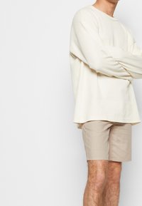 Lichtbeige geribbelde shirt met lange mouwen en brede manchetten, gecombineerd met lichtbruin shorts met een subtiel ruitpatroon.
