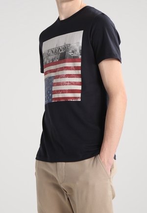 Marineblaues Baumwoll-T-Shirt mit einem Grafikdruck einer amerikanischen Flagge und einer Stadtsilhouette sowie dem Schriftzug "UNION 90" auf der Vorderseite. Kurzärmlig.