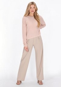 Lichtroze gebreide trui met lange mouwen, gecombineerd met lichtbeige wijde broekspijpen en beige sandalen met hak, staand tegen een neutrale achtergrond.