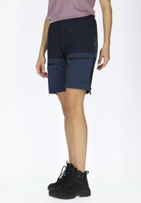 Pantaloni corti della marina con numerose tasche con zip, pannelli blu scuro a contrasto e un design snello. Abbinati a scarponi da trekking neri.