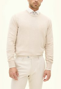 Beige Strickpullover mit Rundhalsausschnitt, gerippten Bündchen, kombiniert mit hellbeigen Hosen. Glatte Textur, taillierte Passform, minimalistischeres Design.