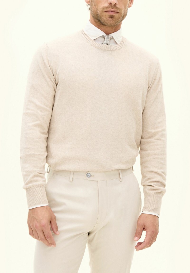 Beige Strickpullover mit Rundhalsausschnitt, gerippten Bündchen, kombiniert mit hellbeigen Hosen. Glatte Textur, taillierte Passform, minimalistischeres Design.