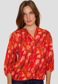 Rode, gemusterde blouse met V-hals, knoopsluiting en ballonmouwen; gemaakt van lichtgewicht stof met abstracte vormen in oranje en roze.