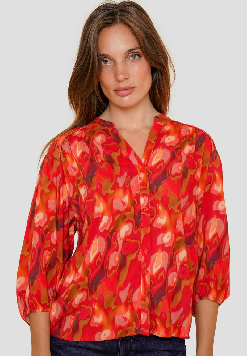 Rode, gemusterde blouse met V-hals, knoopsluiting en ballonmouwen; gemaakt van lichtgewicht stof met abstracte vormen in oranje en roze.