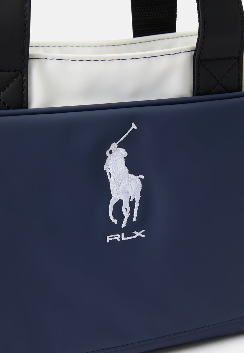Bolso tote azul marino fabricado en material suave, con un logotipo bordado y acentos blancos. El interior es blanco; la parte superior es estructurada con asas negras.