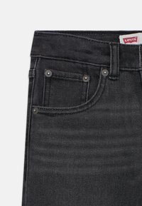 Čierne denimové nohavice s klasickým dizajnom, dvoma prednými vreckami s kovovými cvokmi a štítkom Levi's na páse. Hladká textura.