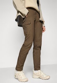 Brown cargo pants with multiple pockets, tapered fit, and reinforced seams. Paired with light-colored athletic shoes.
