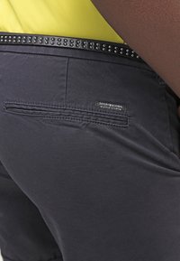 Pantalones cortos de color marino hechos de algodón con una textura suave, que presentan una cinturilla negra con tachuelas y una pequeña etiqueta con la marca "Scotch & Soda".