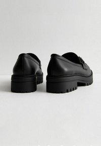 Zapatos de cuero negro con corte bajo y suela de goma gruesa, con un acabado texturizado y un diseño de puntera redonda.
