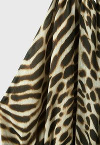 Tissu fluide avec un motif animalier noir et marron ressemblant à des taches de zèbre et de léopard sur fond beige clair.