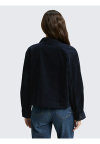 Marineblauwe corduroy jas met een kraag, lange mouwen en knopenmanchetten. Gekort ontwerp met een ontspannen pasvorm en minimalistische stikdetails.