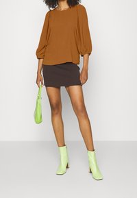 Haut marron à manches bouffantes associé à une mini-jupe moulante en maille côtelée marron foncé. Accessoirisé d'un sac vert clair et de bottines vertes brillantes.