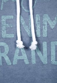 Mörkblå sweatshirt i tyg med ljusgrön sliten text och vita snören med fluffiga ändar.