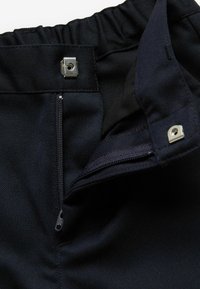 Pantaloni corti neri in tessuto con vita elastica, dotati di chiusura a scatto in metallo, cerniera visibile e texture liscia.