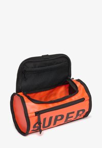 Oranje cilinderzak met zwarte accenten, ritssluiting en een voorklep. Het interieur heeft een effen textuur met een mesh ritszak.