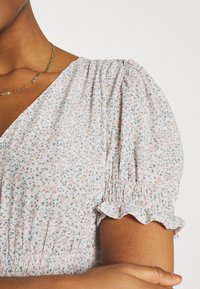 Vestido floral rosa claro com detalhes em verde, apresentando mangas bufantes e punhos com babados. Tecido suave com um corte descontraído. Detalhe de cintura elástica.