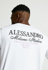 Biela tričko s odvážnym čiernym a svetlofialovým textom na chrbte, na ktorom sú napísané mená "ALESSANDRO Milano Italia" a "PIAZZA DUCA D'AOSTA."