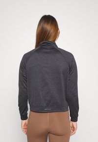 Svart långärmad sporttop med hög krage och raglanärmar, tillverkad av textilier med struktur, med en diskret logotyp längst ner.