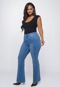 High-waisted, uitlopende jeans in middelblauwe denim met een gladde textuur en een metalen knoop. Gecombineerd met een aansluitend zwart topje met een ronde hals.