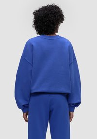 Niebieski, oversize'owy sweter z szerokimi rękawami i ściągaczem u szyi, wykonany z miękkiego materiału. Zestawiony z dopasowanymi niebieskimi spodniami.