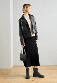 Veste en cuir noir de motard, top en tricot beige, jupe midi à côtes noires, et bottines noires à lacets. Accessoire : petit sac à main noir avec chaîne.