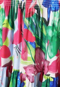 Tejido con patrón floral que presenta grandes flores rosas, rojas y verdes sobre un fondo azul claro con un diseño plisado. Textura suave.