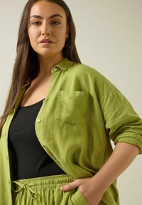 Linnen groene shirt met kraag, voorzak en knoopsluiting, gecombineerd met een zwarte top en bijpassende groene broek met een trekkoord in de taille.