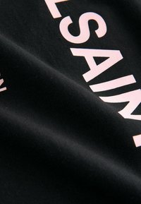 Melna auduma ar maigu tekstūru, uz kura virsmas ir lieli, gaiši rozā burti, kas uzrakstīti "SAINT LAURENT".