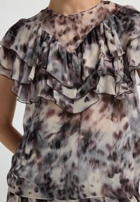 Top trasparente con volants a strati, caratterizzato da un motivo ad acquerello in tonalità di marrone, beige e grigio, con una texture morbida e leggera.