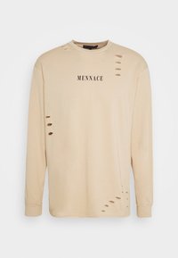 Beige košile s dlouhým rukávem a kulatým výstřihem, s několika poškozenými výřezy, přední nápis "MENNACE" a žebrované manžety. Hladká bavlněná textura.