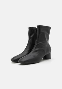 Bottines noires en cuir lisse avec un bout pointu, fermeture éclair et un talon bloc de hauteur intermédiaire. Design minimaliste avec des coutures subtiles.