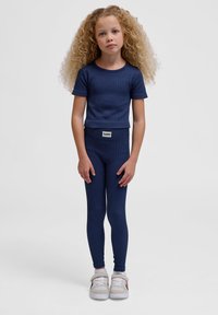 Marineblå ribbet kortærmet top og matchende leggings med en tætsiddende pasform. Sættet suppleres af hvide sneakers med grå detaljer.