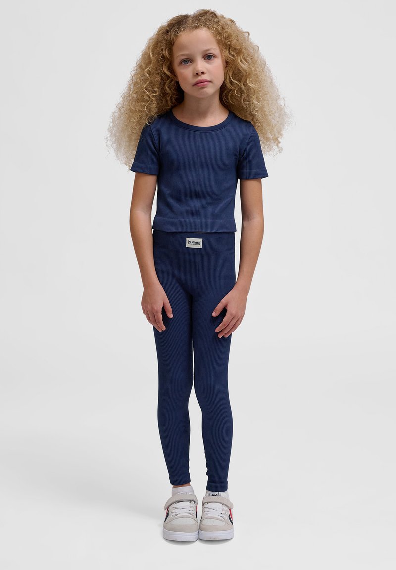 Marineblå ribbet kortærmet top og matchende leggings med en tætsiddende pasform. Sættet suppleres af hvide sneakers med grå detaljer.
