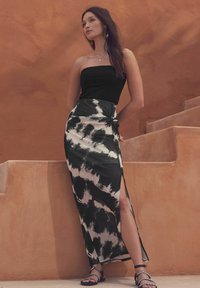 Melns bezplecu tops, kombinēts ar garu melnbaltu tievās krāsas maksi svārku ar sānu šķēlumu. Modelis valkā plakanu sandaļu ar ķēdes akcentiem.